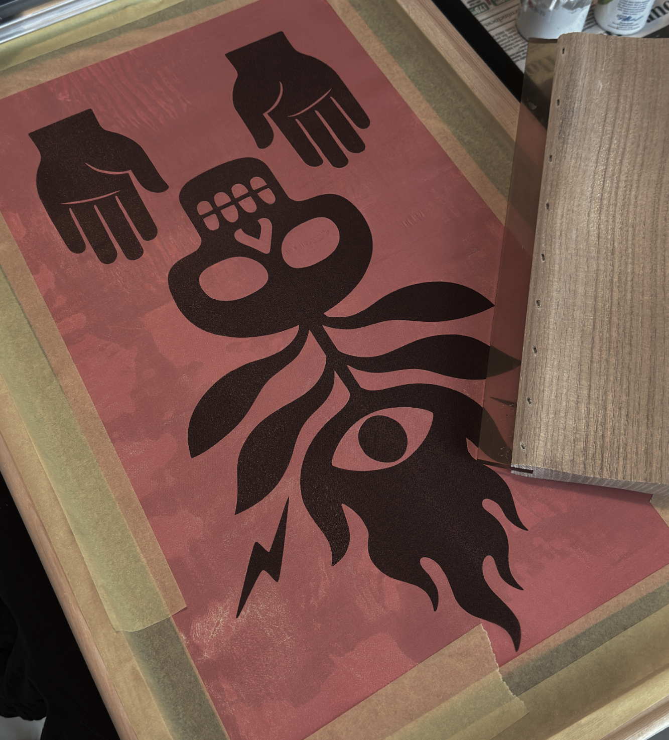 Silk Screen print with flambos totem  on a red background, placed on a wooden surface.